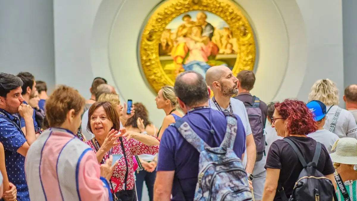 Tour guide speaking to a group of visitors in front of a famous circular painting at the Uffizi Gallery in Florence.