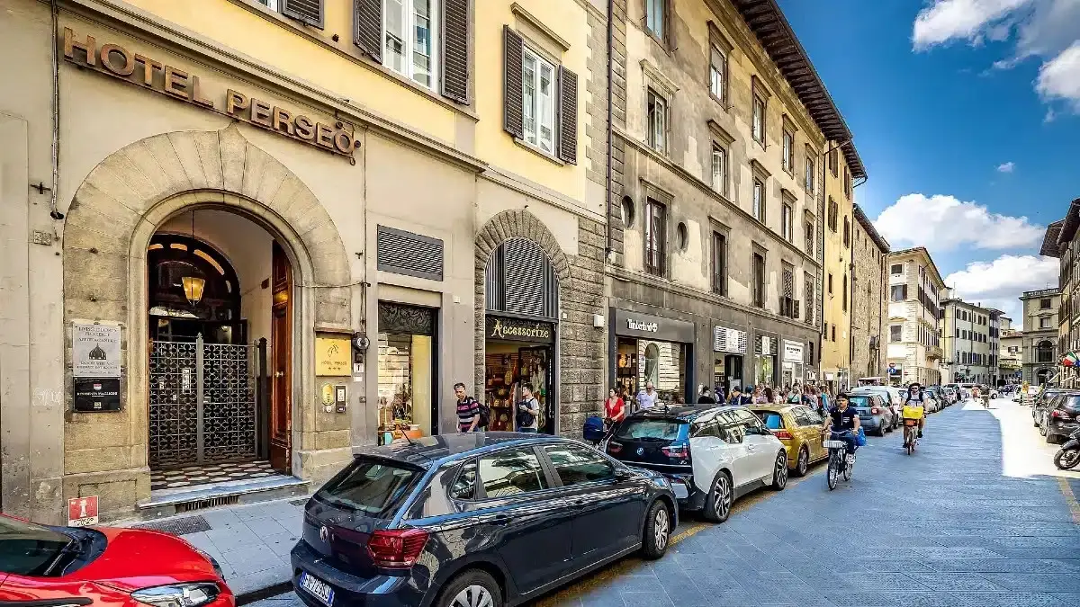 Street near Florence’s Duomo with Hotel Perseo, parked cars, people walking, and cyclists.