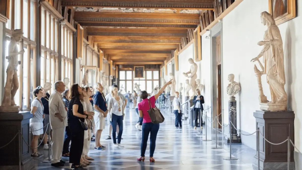 Tour guide showing a group of visitors around a statue-filled hallway inside the Uffizi Gallery in Florence.